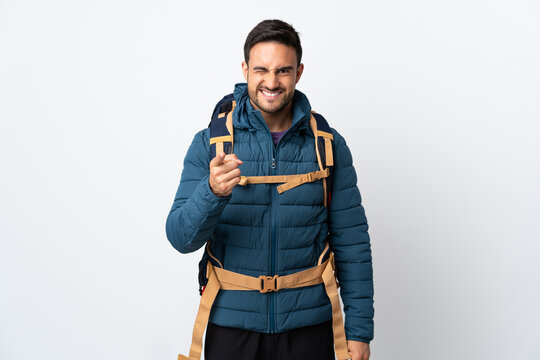 Young mountaineer man with a big backpack isolated on white background points finger at you