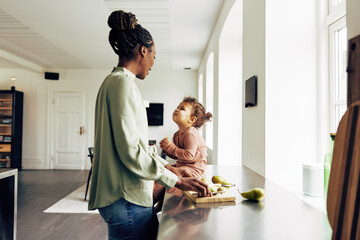 Mom and her cute little daughter eating fruit at home