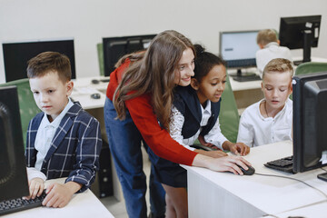Obraz premium Children learns to work on a computer. African girl sitting at the table. Boys and girl in computer science class.