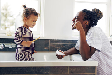 Mom showing her smiling little daughter how to brush her teeth