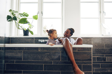 Smiling mom teaching her little daughter how to brush her teeth