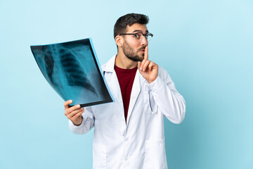 Professional traumatologist holding radiography isolated on blue background doing silence gesture