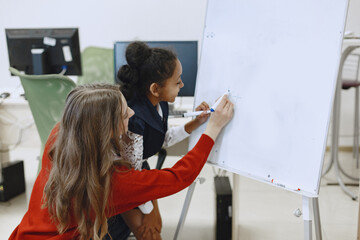 Child in computer science class. African girl standing near school board for presentation. Teacher with her student.