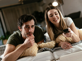 Young loving couple relaxing on sofa together. Happy couple watching movie at home.