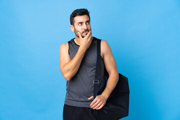 Young sport man with sport bag isolated on blue background having doubts and with confuse face expression