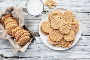 Flatlay of fresh baked, homemade peanut butter cookies and milk over a white rustic table. Image shot from up above, top view.