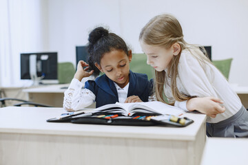 African girl sitting at the table. Schoolgirls read a book during a break. Children sit in a computer science class.