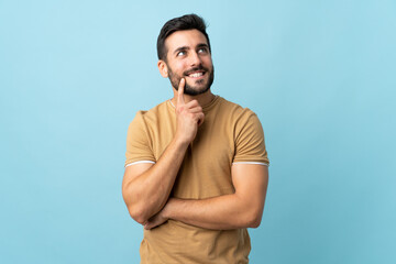Young handsome man with beard over isolated background thinking an idea while looking up