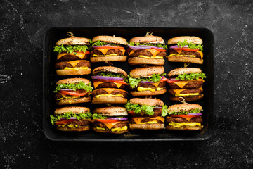 Delicious grilled homemade burgers with beef, tomatoes, cheese, onions and salad. Burger menu. Top view. On a black stone background.
