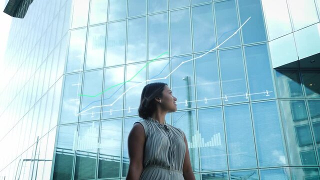 Business woman model looks at positive trend diagram on glass financial building. Rising trend, stock market, price development