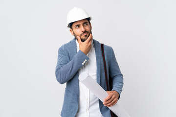 Young architect man with helmet and holding blueprints isolated on white background having doubts