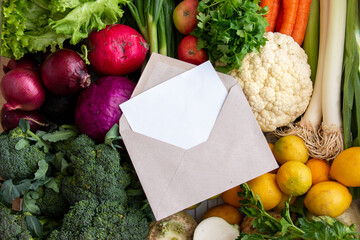 White paper and letter envelope on various organic vegetables for healthy eating. harvest of broccoli, cauliflower, leek, purple onion, cabbage, lemon, celery.