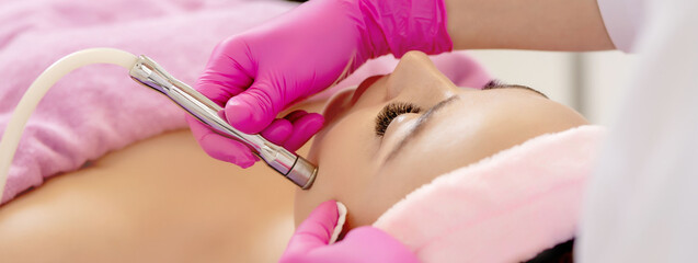 The cosmetologist makes the procedure Microdermabrasion of the facial skin of a beautiful, young...