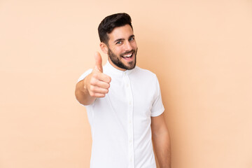 Caucasian handsome man isolated on beige background with thumbs up because something good has happened