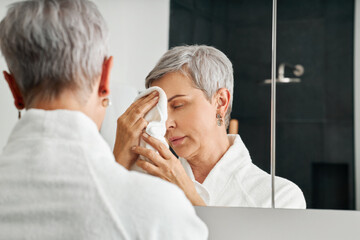 Mature woman standing in front of a mirror in bathroom doing a morning skincare routine