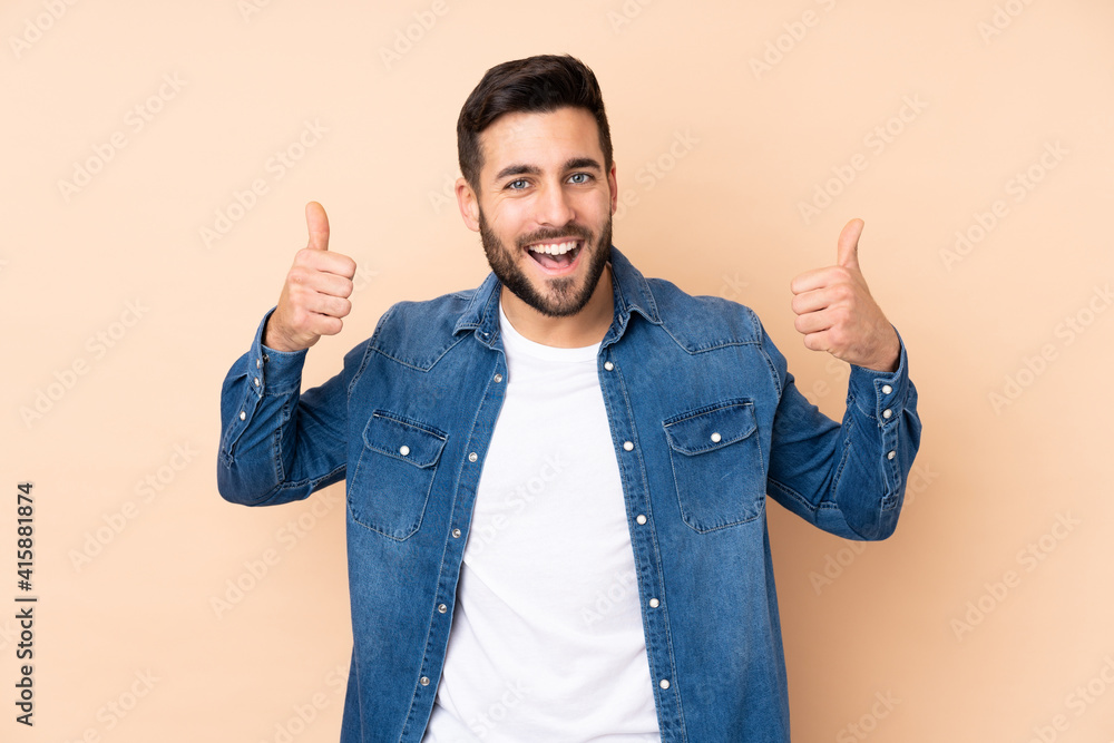 Wall mural caucasian handsome man isolated on beige background giving a thumbs up gesture