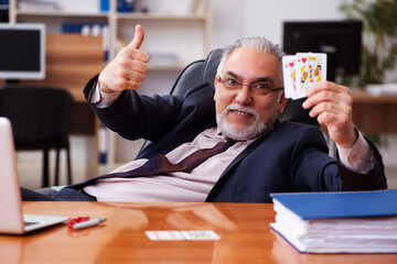 Old male employee playing cards at workplace