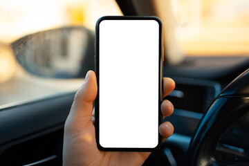 Close-up of male hand holding smartphone with white mockup on screen against blurred background of car interior.