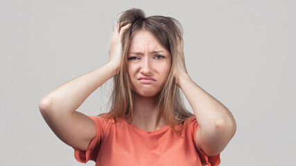 Portrait of young blond woman in panic grabbing her head in fear or frustration. Stress and mental health