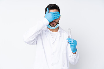 Dentist man holding tools isolated on white background covering eyes by hands