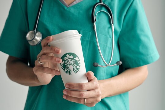 Female Doctor Holding Starbucks Coffee Cup And Using Mobile Phone