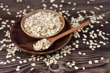 Oat flakes uncooked in wooden bowl with spoon on a dark wooden table. Concept of healthy eating