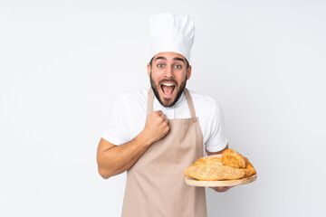 Male baker holding a table with several breads isolated on white background celebrating a victory