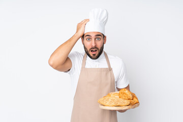 Male baker holding a table with several breads isolated on white background with surprise facial expression