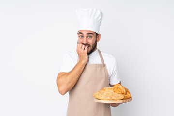 Male baker holding a table with several breads isolated on white background nervous and scared