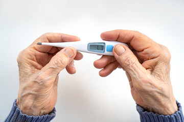 Old wrinkled hands holding an electronic thermometer for body temperature measurement