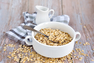 Oat flakes uncooked in a white bowl on rustic table. Healthy food for breakfast