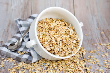 Oat flakes uncooked in a white bowl on rustic table. Healthy food for breakfast