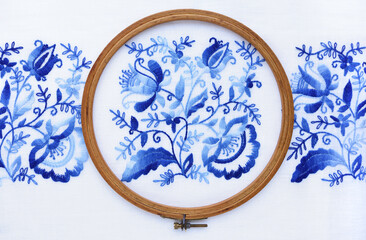 Embroidery hoop with fabric, top view. Blue floral ornament on a white background