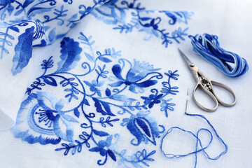 Embroidery, thread and scissors. Blue floral ornament on a white background. Art and craft conception.