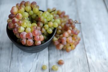 Colored grapes in a black bowl on a gray wooden table,nearby branch of red grape