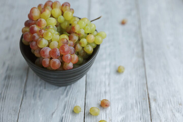 Still life with colored grapes in a bowl on a gray wooden table in day light.