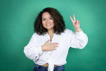 Young african american girl wearing white shirt over green background smiling swearing with hand on chest and fingers up, making a loyalty promise oath