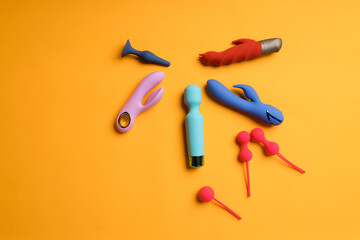 An abundance of multi-colored dildos and kegel balls on a yellow background. Clitoris massager, sex toys to maintain women's health. Space for text
