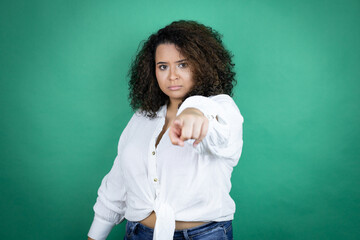 Young african american girl wearing white shirt over green background pointing with finger to the camera and to you, confident gesture looking serious