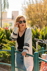 Young woman wearing stylish sunglasses and white sweater in park