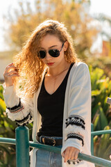 Young woman wearing stylish sunglasses and white sweater in park