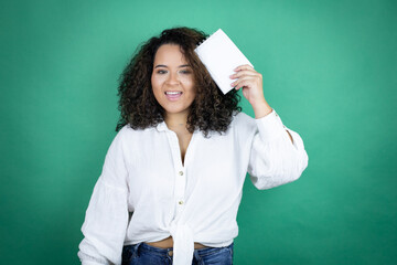 Young african american girl wearing white shirt over green background smiling and showing blank notebook in her hand
