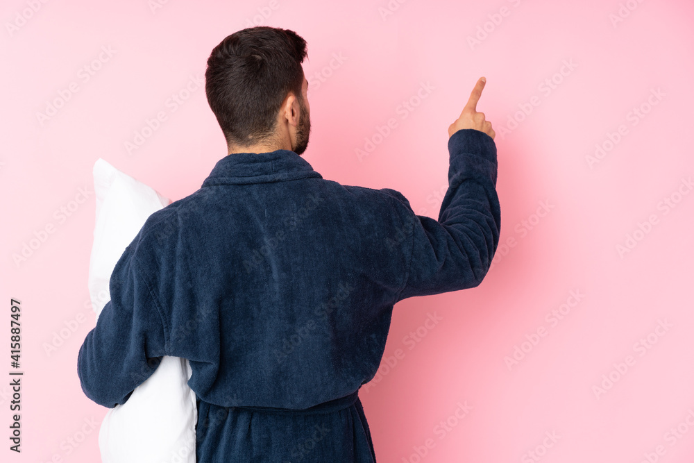 Wall mural young man going to sleep isolated on pink background pointing back with the index finger