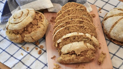Round loaves of rustic bread on a blue and white square patterned dishcloth with two of the loaves cut into slices