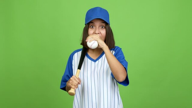 Young brunette woman doing surprise gesture and playing baseball over isolated background. green screen chroma key