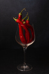 Chili peppers in a glass on a black background. Dark photo.