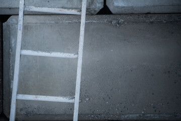 close up partial view of ladder leaning against cement concrete block wall on construction site in urban industrial area shades of grey horizontal format space for type straight and angles lines 