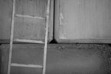 close up partial view of ladder leaning against cement concrete block wall on construction site in urban industrial area shades of grey horizontal format space for type straight and angles lines 