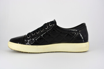Stylish bright black lacquer shoes located on a white background. Moccasins made of genuine leather with bullshit and black wide laces. Women's sneakers on a white tast sole. 