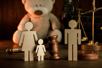 Wooden figures of family with teddy bear and gavel on a table close-up. Divorce and alimony concept.
